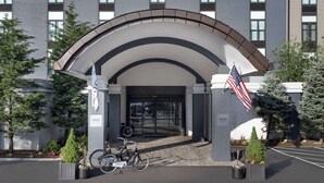 A modern building with a curved entrance, American flags, and a bicycle parked outside. - Freepoint Hotel Cambridge, Tapestry Collection by Hilton (Cambridge)