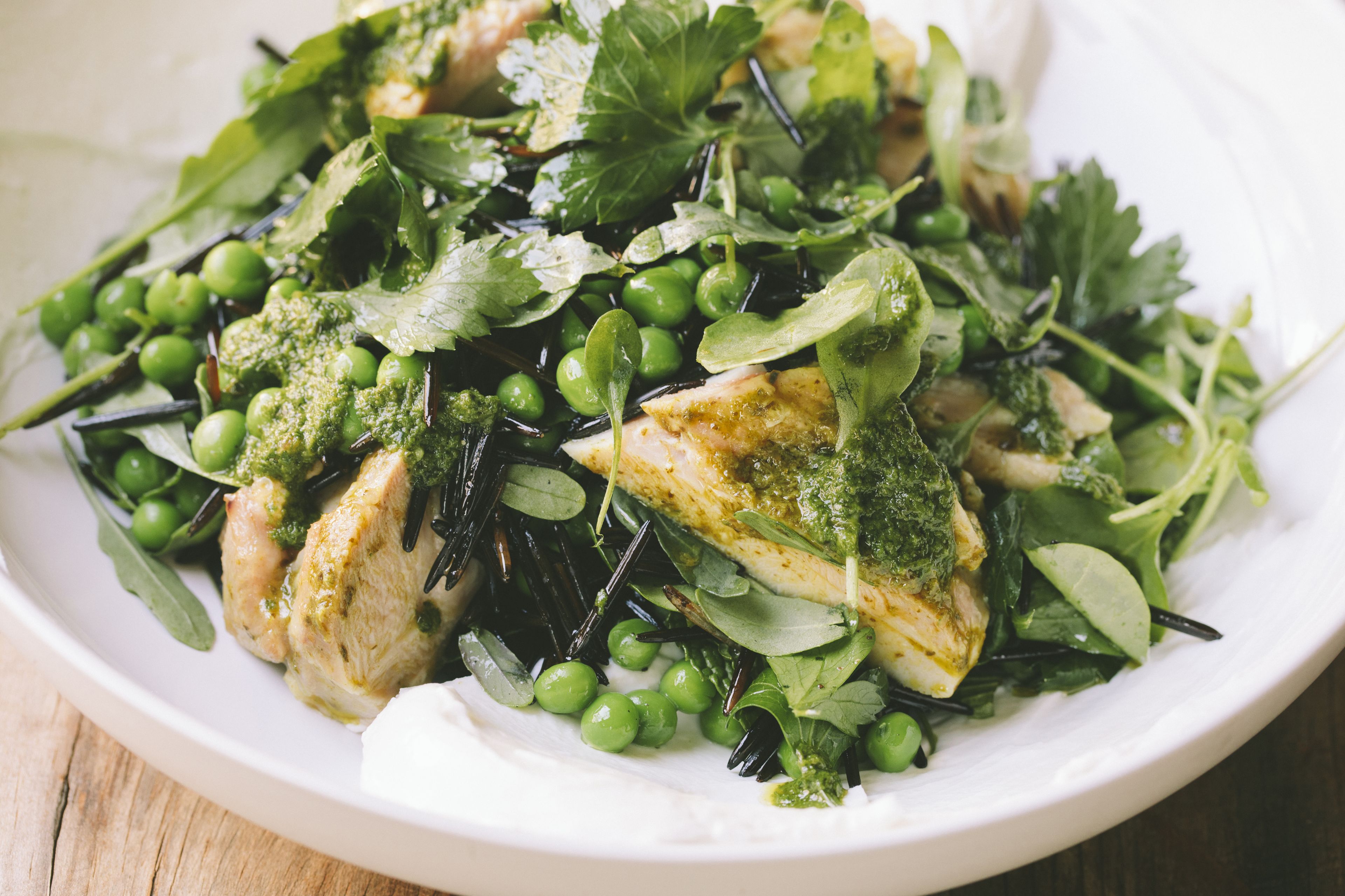 A white plate with a salad containing greens, peas, and a piece of chicken.