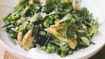 A white plate with a salad containing greens, peas, and a piece of chicken.