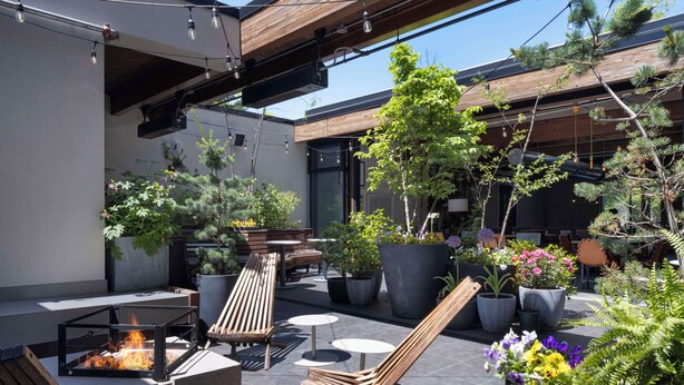 An outdoor patio with wooden furniture, potted plants, and a fire feature. - Freepoint Hotel Cambridge, Tapestry Collection by Hilton (Cambridge)