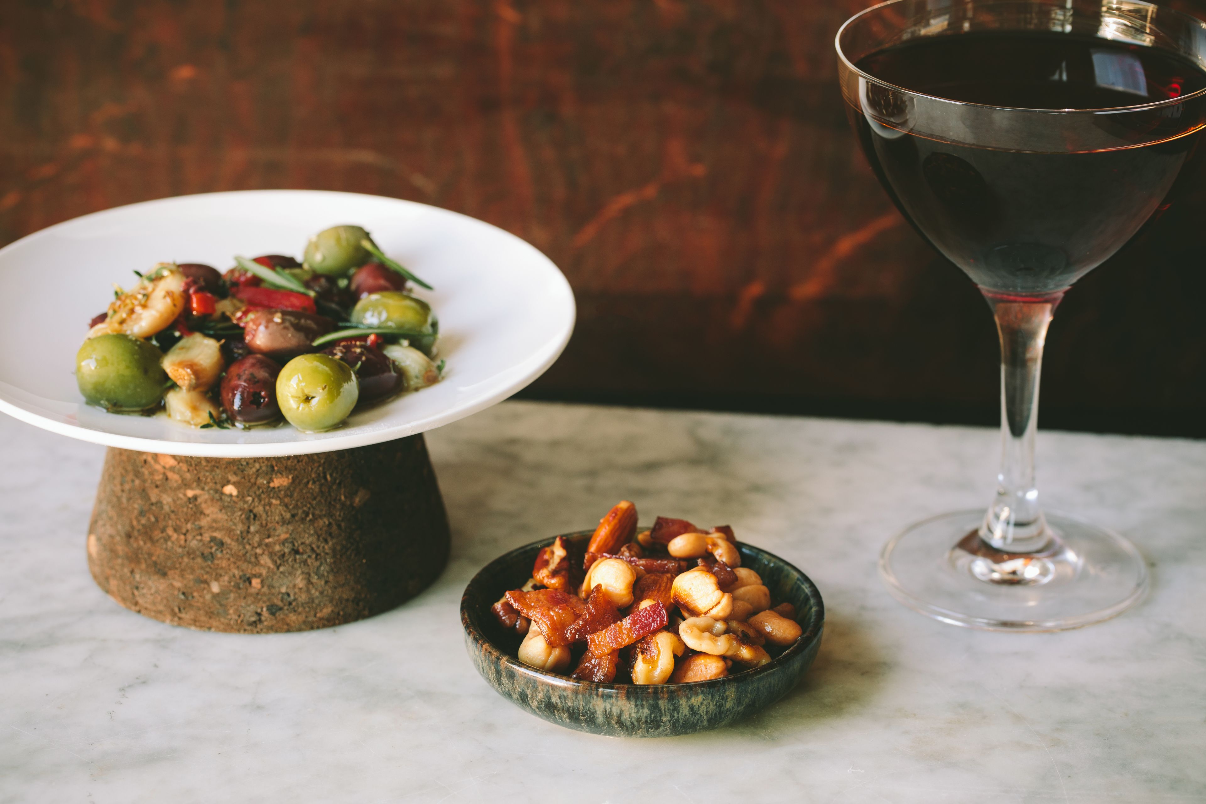 A plate of food with olives and nuts, a bowl of nuts, and a wine glass.