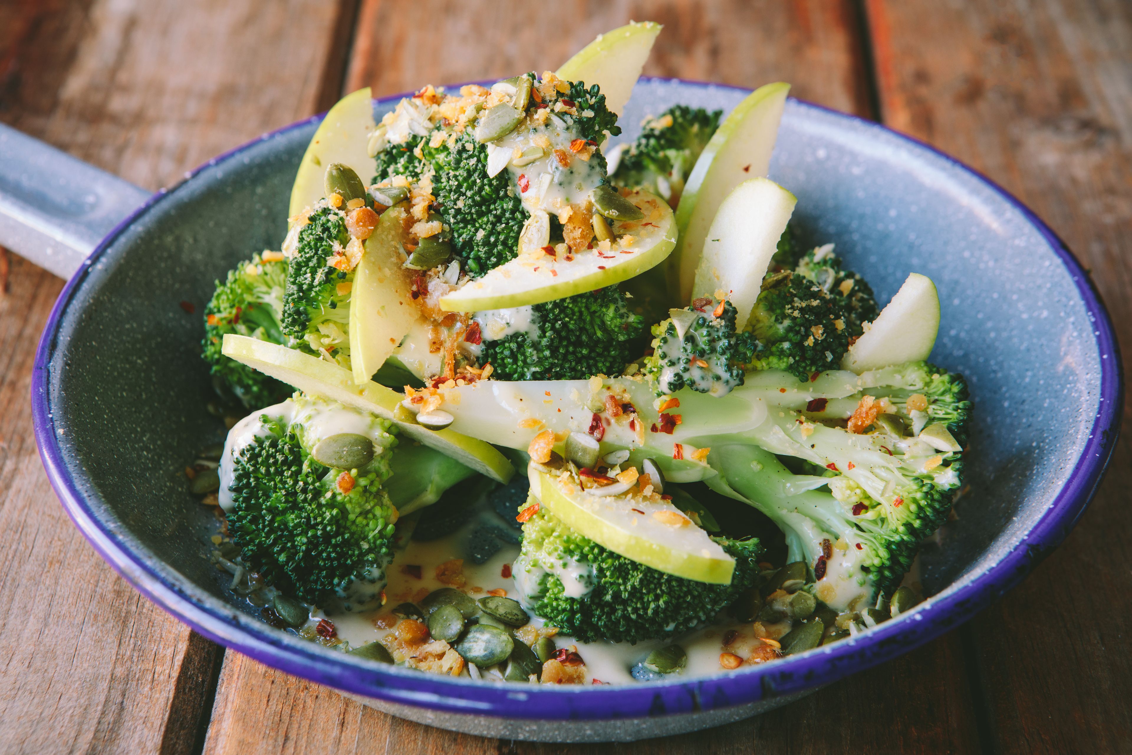 A bowl of broccoli and apple slices with a creamy sauce, garnished with seeds and spices.