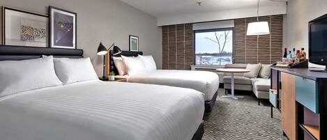 Habitación de hotel con dos camas, un escritorio, una silla, un televisor y una ventana con persianas.