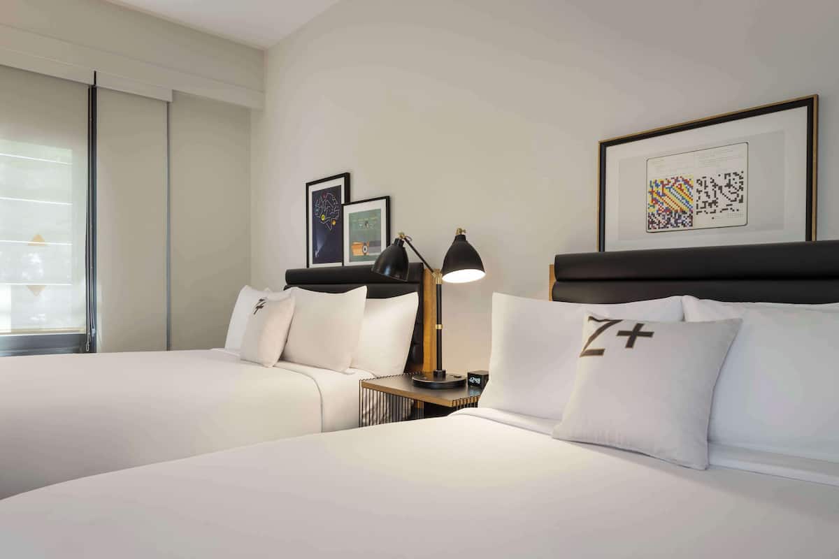 A hotel room with two beds, a nightstand with a lamp, and framed artwork on the walls.