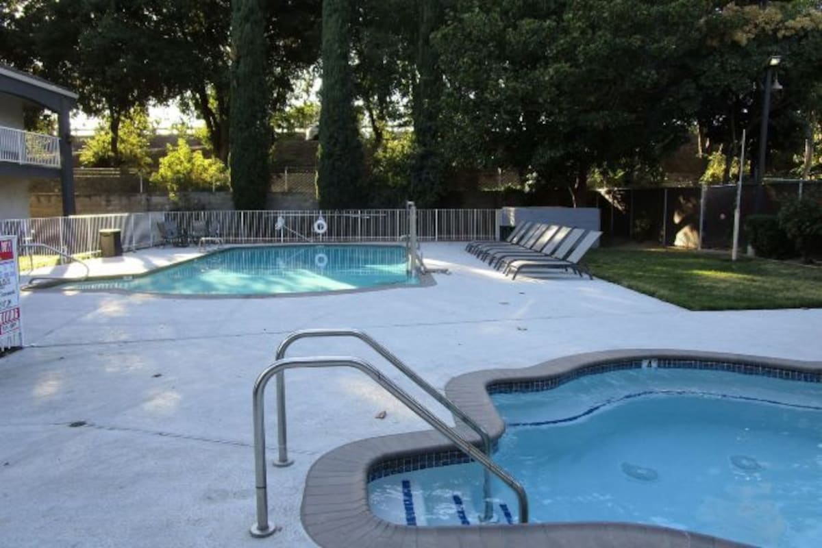 A swimming pool with a small hot tub, surrounded by a white fence and lounge chairs.