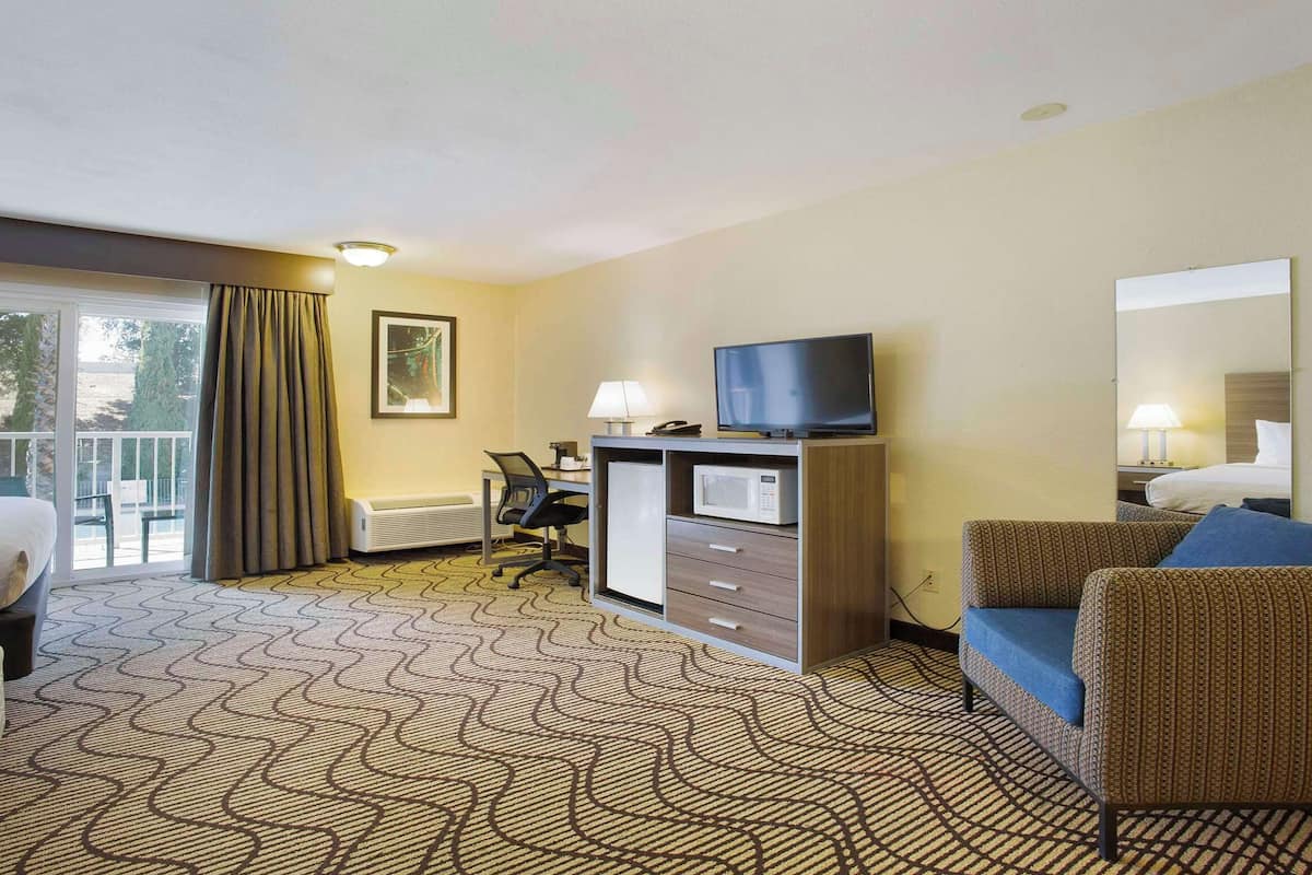 A hotel room with a bed, a desk with a computer, a chair, a television, and a large window with curtains.