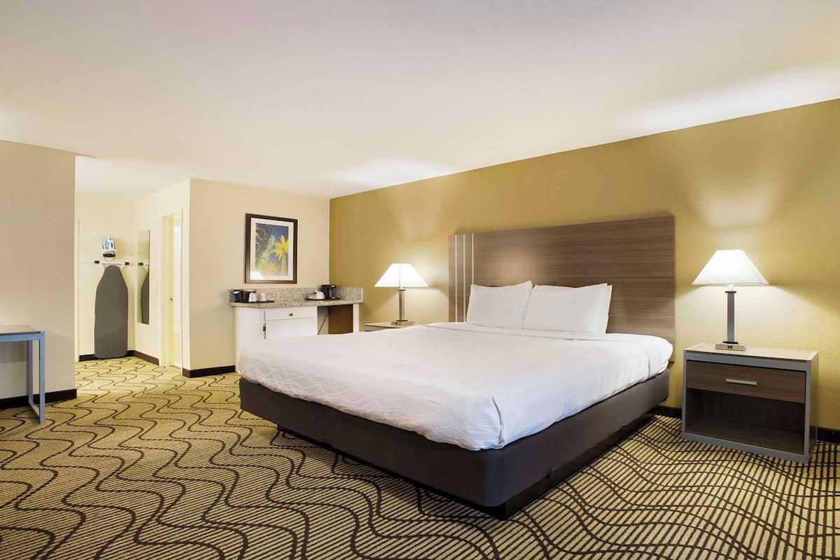 A hotel room with a large bed, two bedside tables with lamps, a desk with a chair, and a bathroom in the background.