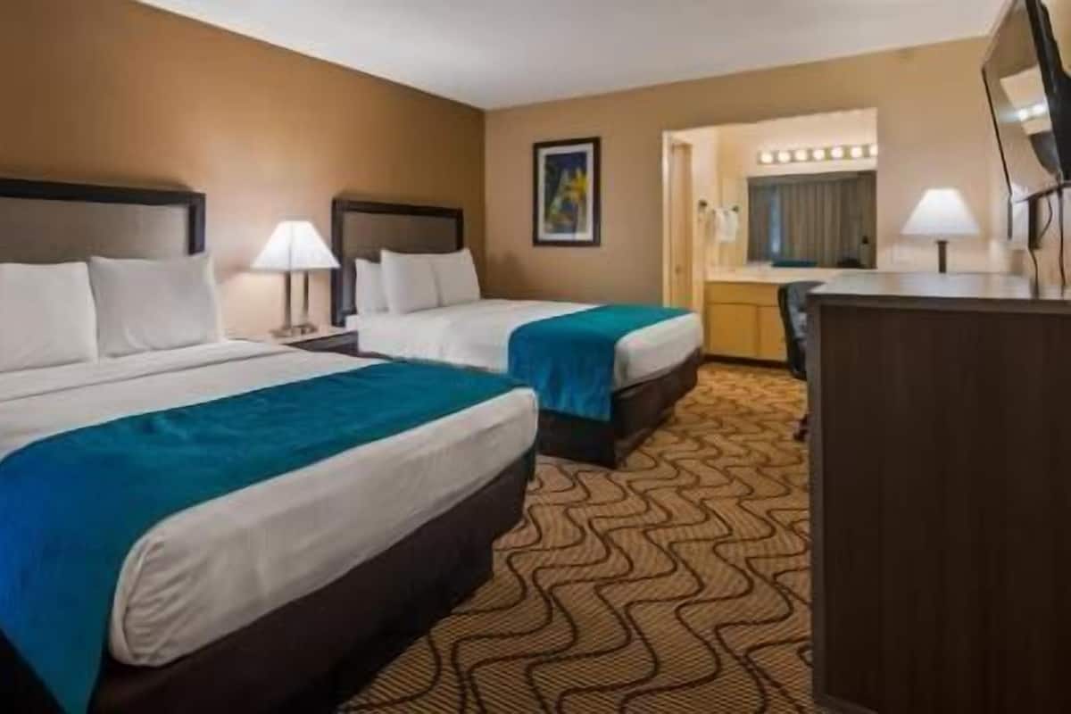 A hotel room with two beds, a desk, and a mirror.