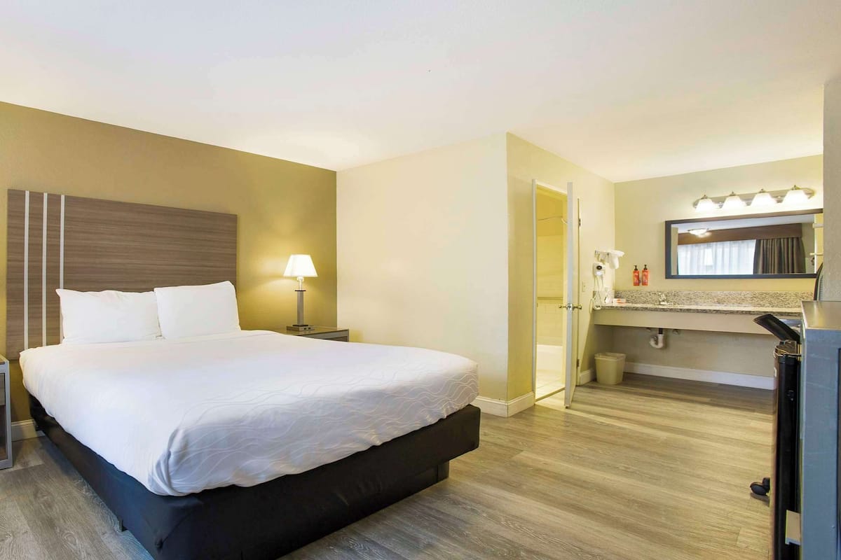 A hotel room with a bed, bedside tables, a nightstand, a mirror, and a bathroom with a sink and mirror.