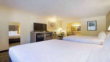 Une chambre d’hôtel avec deux lits, un bureau avec un ordinateur, une télévision, un four à micro-ondes, une petite kitchenette et une salle de bain avec un miroir et un lavabo.