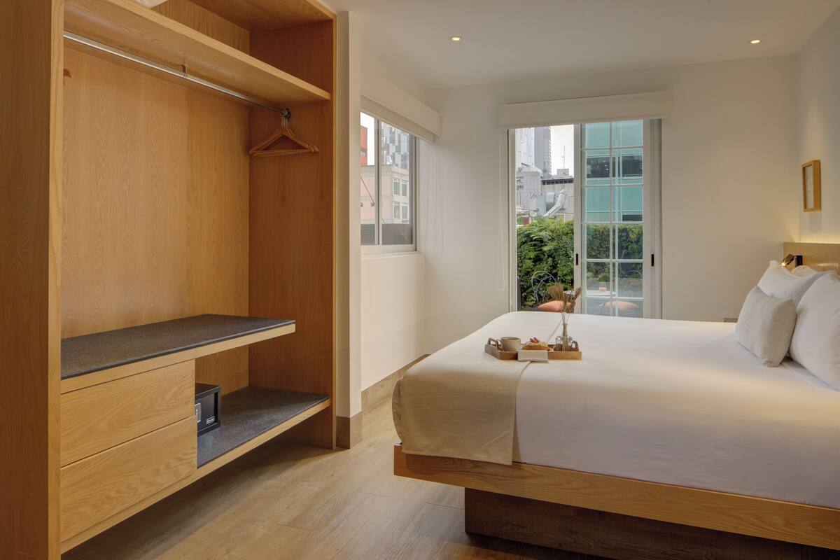 A modern bedroom with a large bed, wooden wardrobe, and a view of the city through a large window.