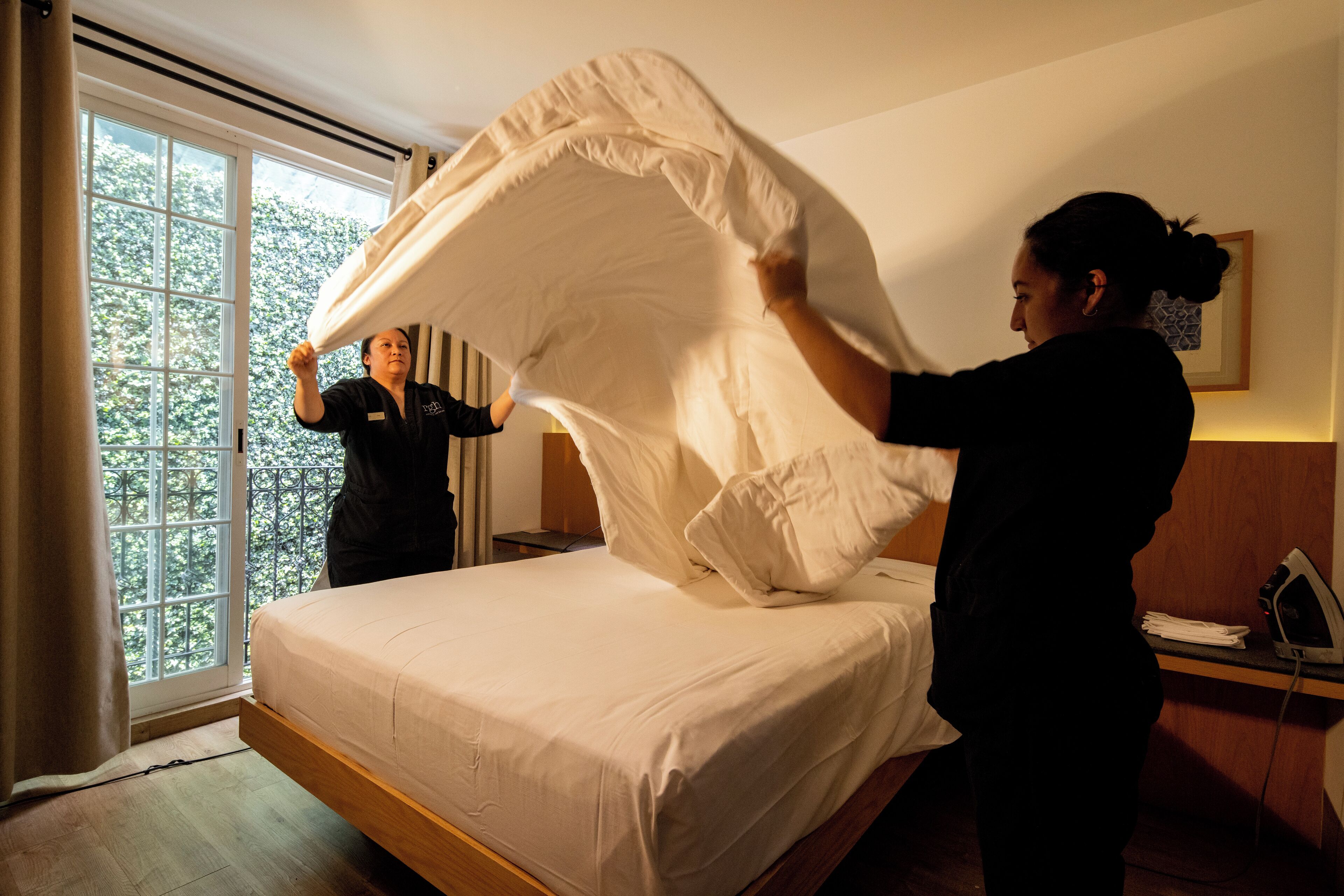 A bedroom with a bed, a window, and a nightstand with an iron.