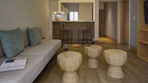 Een moderne woonkamer met een bank, twee barkrukken en drie ronde rieten poefjes.
