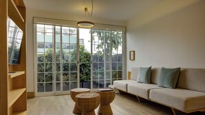 Een moderne woonkamer met een bank, rieten voetenbankjes en een grote schuifpui naar een balkon met planten.