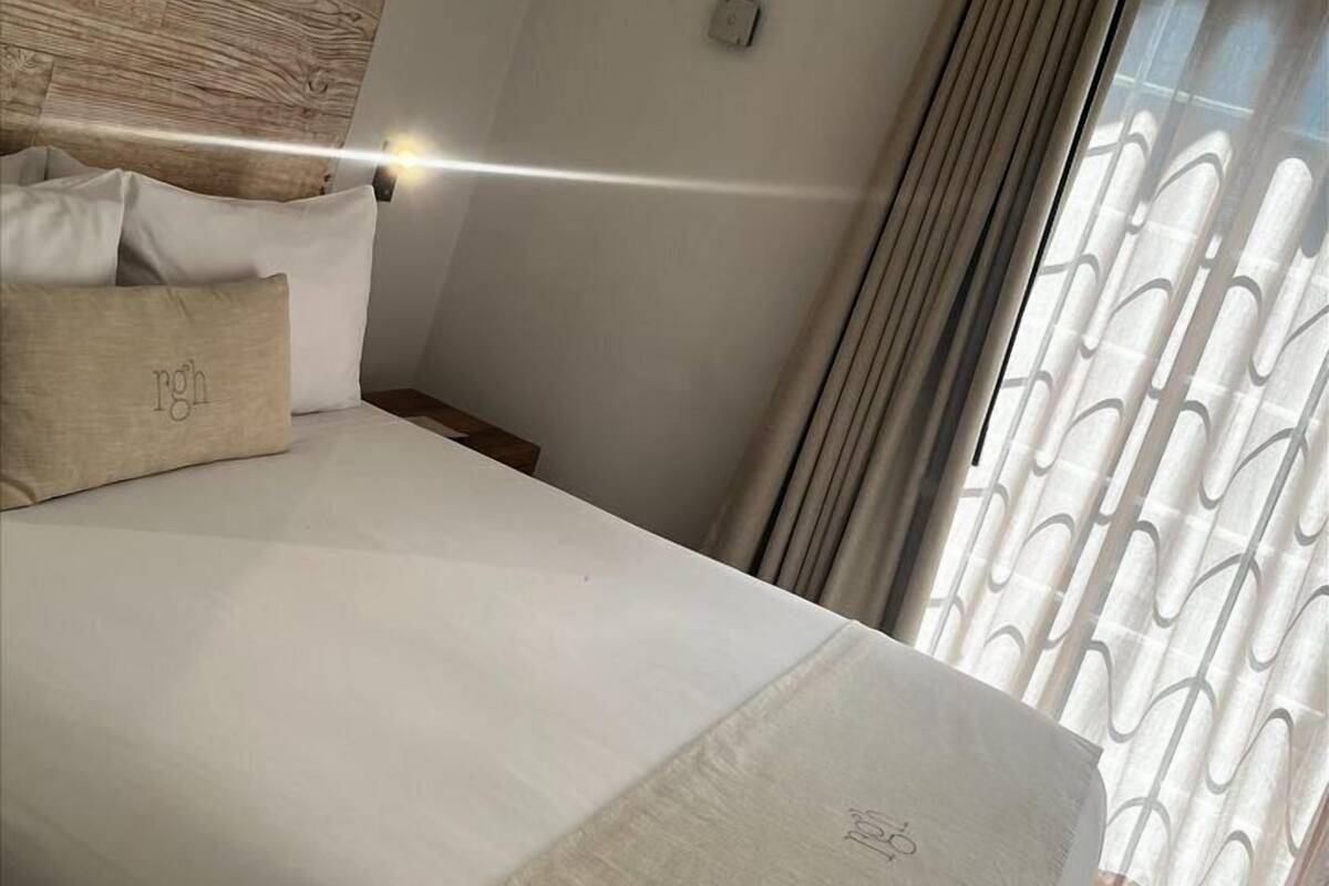 A modern bedroom with a wooden headboard, a bed with white bedding, and a window with patterned curtains.