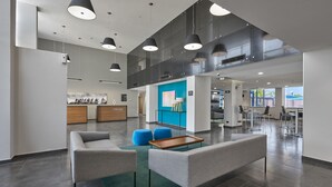 A modern lobby with grey sofas, a wooden coffee table, and blue ottomans. - Hotel Best Place Express (Zamora)