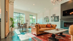 A spacious living room with a leather sofa, a coffee table, and a fireplace. There are framed pictures on the wall and a large window providing natural light. - The Guesthouse Hotel (Chicago)