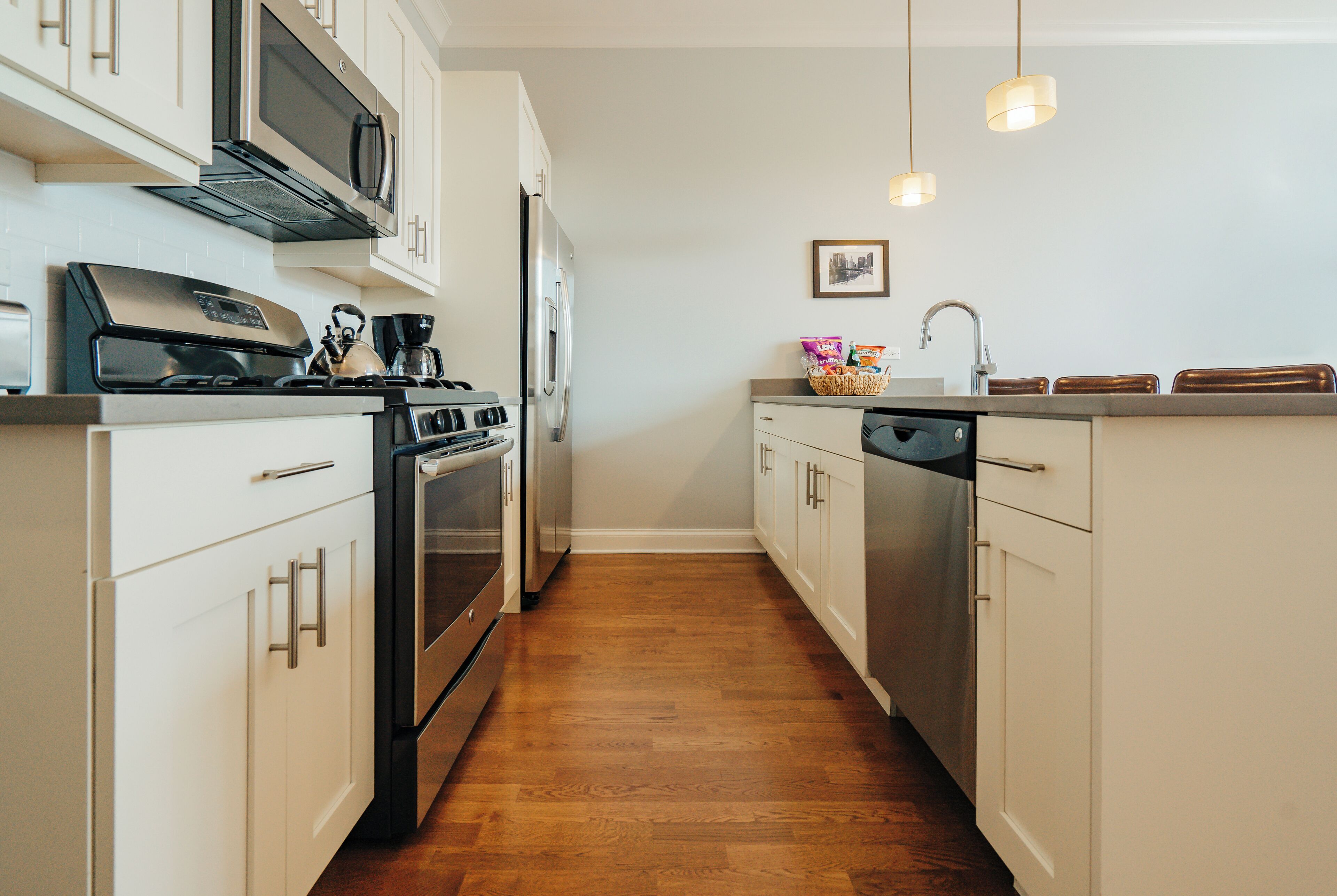 A modern kitchen with stainless steel appliances, white cabinetry, and a wooden floor.