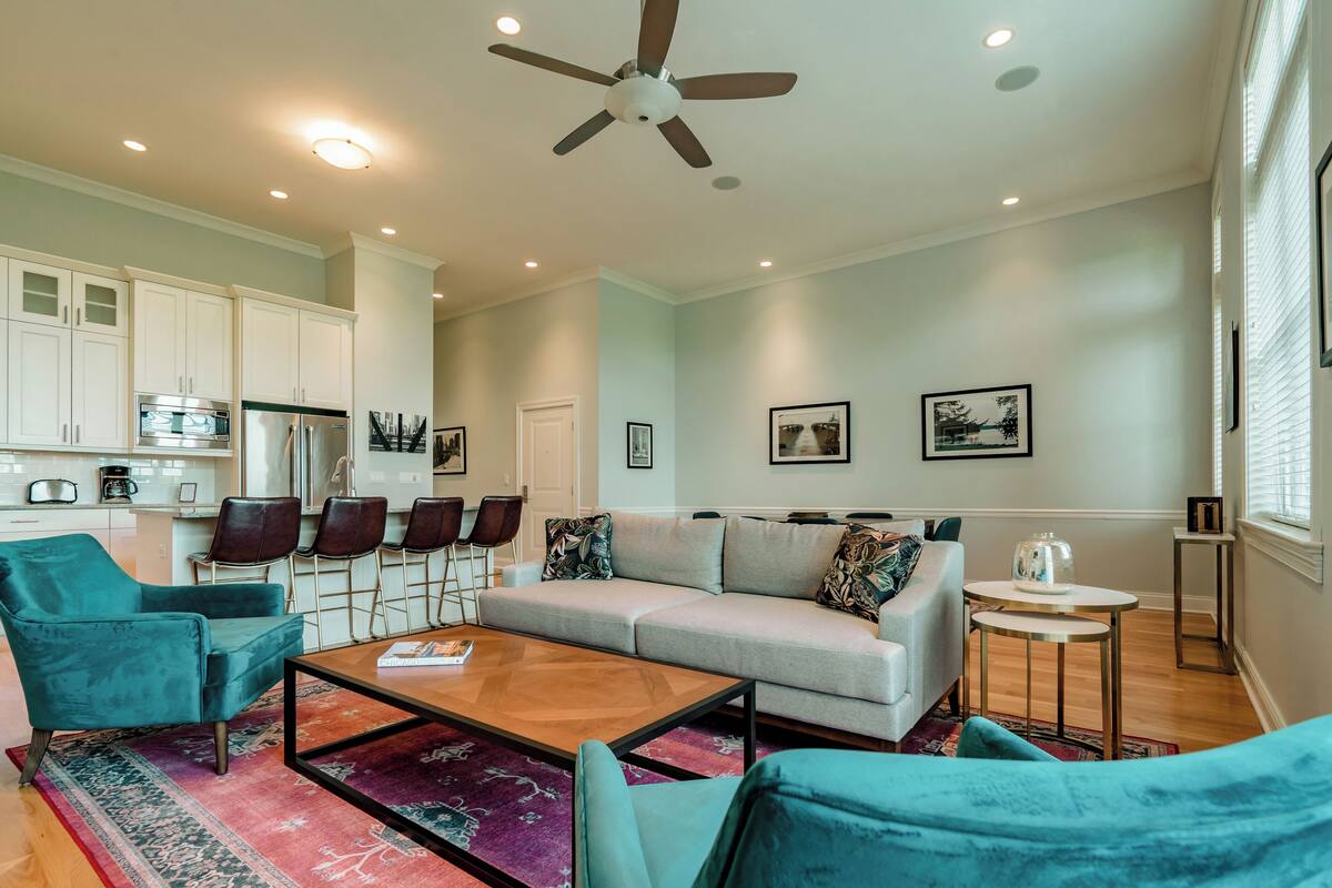 A modern living room with a sofa, armchairs, a coffee table, and a ceiling fan.