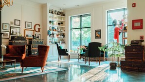 A spacious living room with a large window, a collection of vintage suitcases, and a bookshelf filled with books and decorative items. - The Guesthouse Hotel (Chicago)
