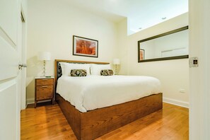 A bedroom with a wooden bed, two bedside tables with lamps, a framed picture on the wall, and a large mirror. - The Guesthouse Hotel (Chicago)