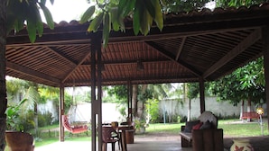 A covered outdoor seating area with a concrete floor, wooden furniture, and a hanging chair. - Pousada das Acacias (São Miguel dos Milagres)
