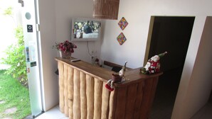 A wooden reception desk with a television mounted above it, a small Christmas decoration, and a vase with flowers. - Pousada das Acacias (São Miguel dos Milagres)