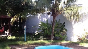 A swimming pool with a brick pathway leading to it, surrounded by greenery and a white wall. - Pousada das Acacias (São Miguel dos Milagres)