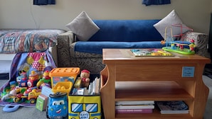 A cozy living room with a blue sofa, a wooden coffee table, and a bookshelf filled with books and toys. - Height of Dunedin (North Taieri)