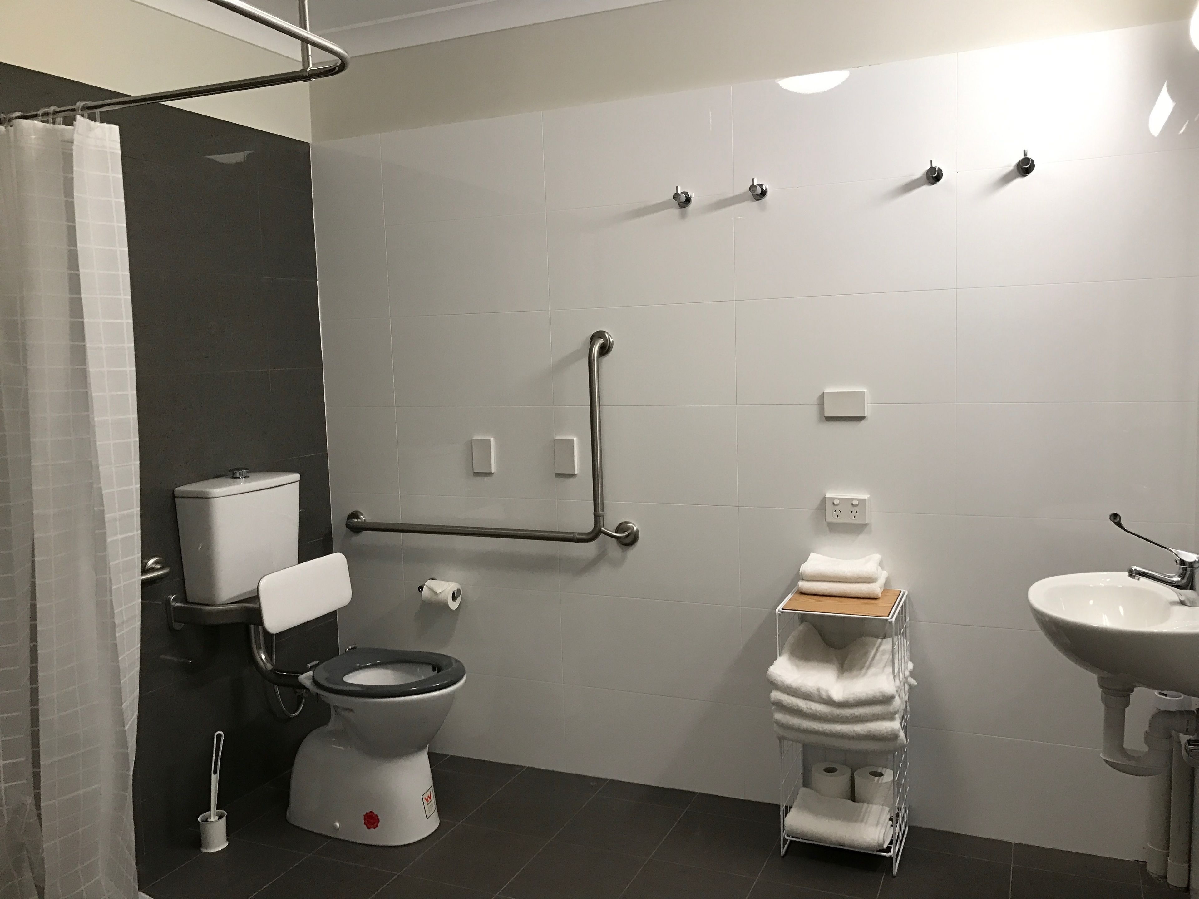 Un baño moderno con inodoro, bidé y lavamanos, equipado con barras de apoyo y un perchero para toallas.