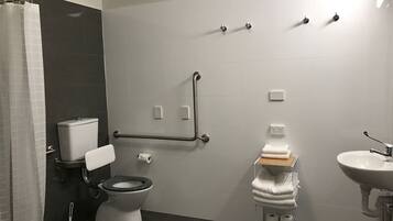 Un baño moderno con inodoro, bidé y lavamanos, equipado con barras de apoyo y un perchero para toallas.