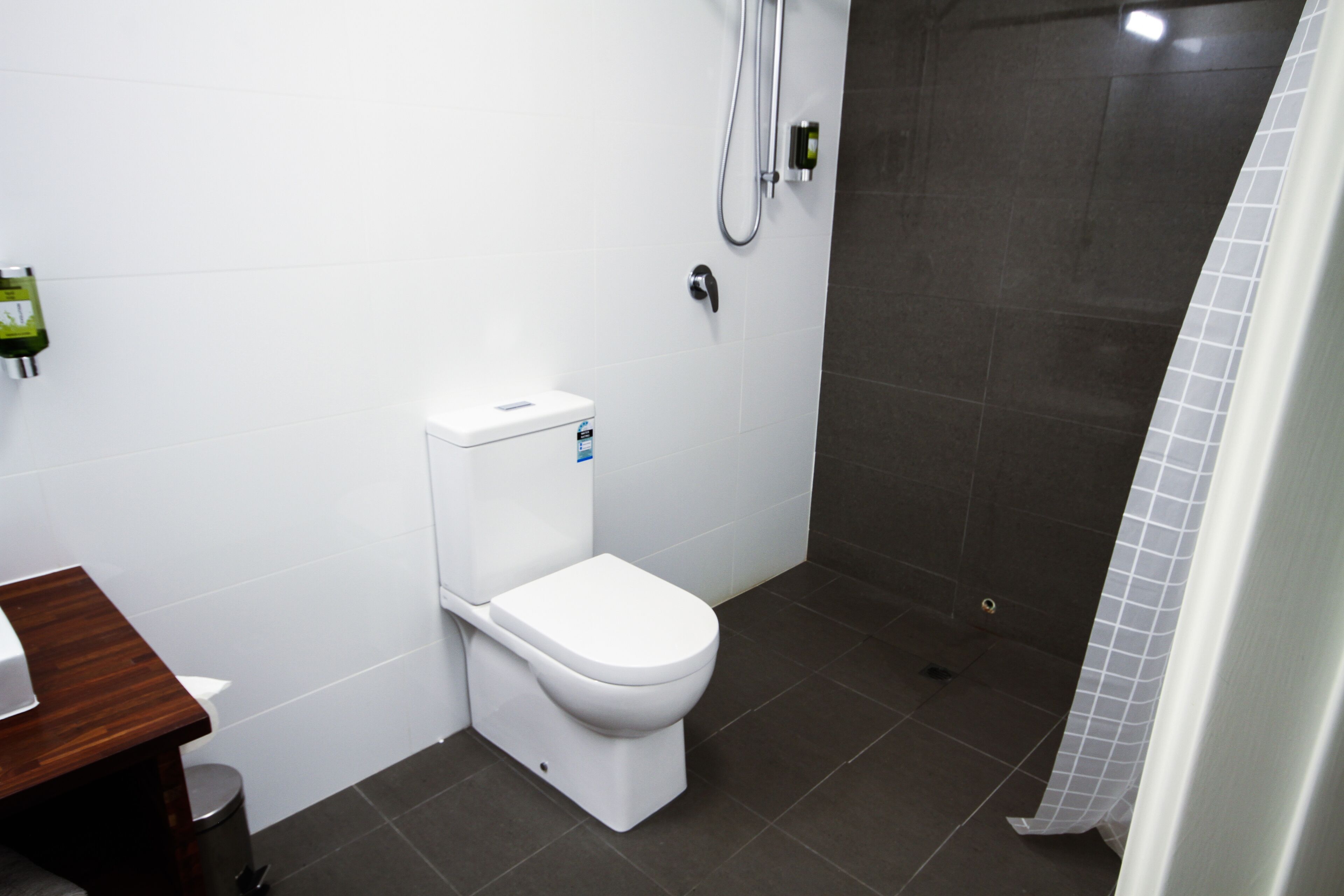 Un baño con inodoro blanco, zona de ducha y suelo de baldosas.