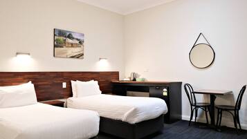 A hotel room with two beds, a desk, a chair, a small table, a mirror, and a painting on the wall.
