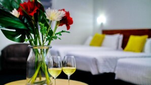A hotel room with a bed, two pillows, a vase with flowers, and two glasses of wine on a round table. - Gallery Hotel (Bibra Lake)