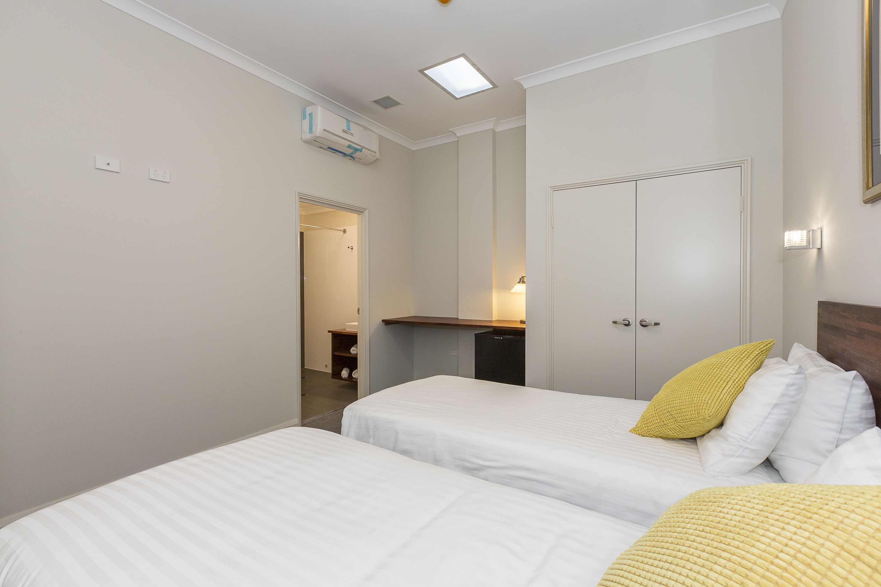 Habitación de hotel con dos camas, un armario, un escritorio y un baño visible a través de una puerta abierta.