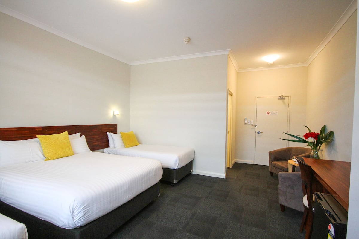 A hotel room with two beds, a desk, a chair, and a small table.