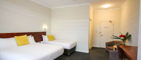 A hotel room with two beds, a desk, a chair, and a small table.