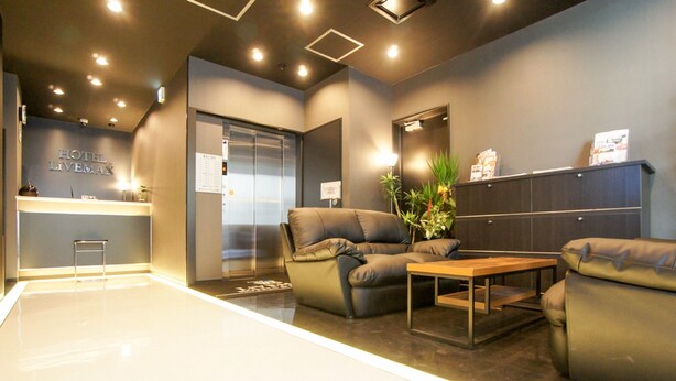 A modern hotel lobby with a reception desk, a seating area with sofas and a coffee table, and a glass elevator. - Hotel LiVEMAX Kayabacho (Tokyo)