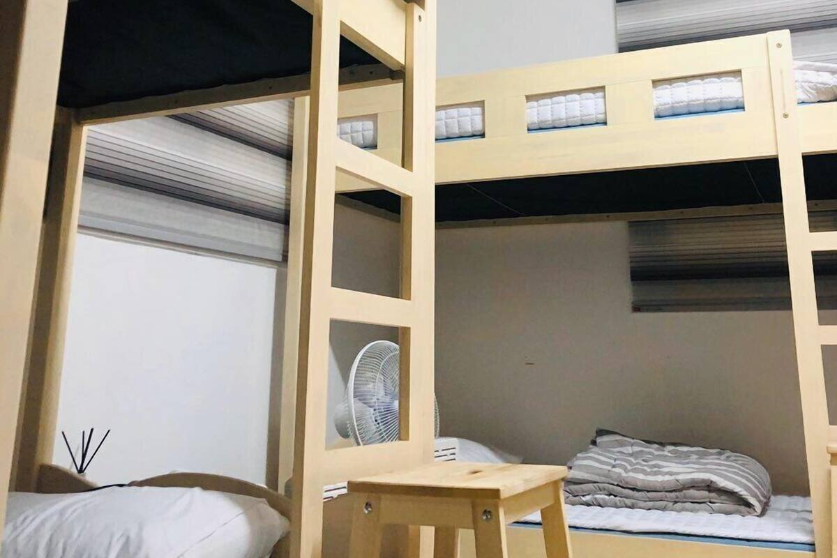 A bunk bed room with a wooden ladder, a small table, and a fan.