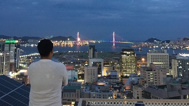A cityscape at dusk with a prominent bridge and illuminated buildings. - Orange Guesthouse - Hostel (Busan)