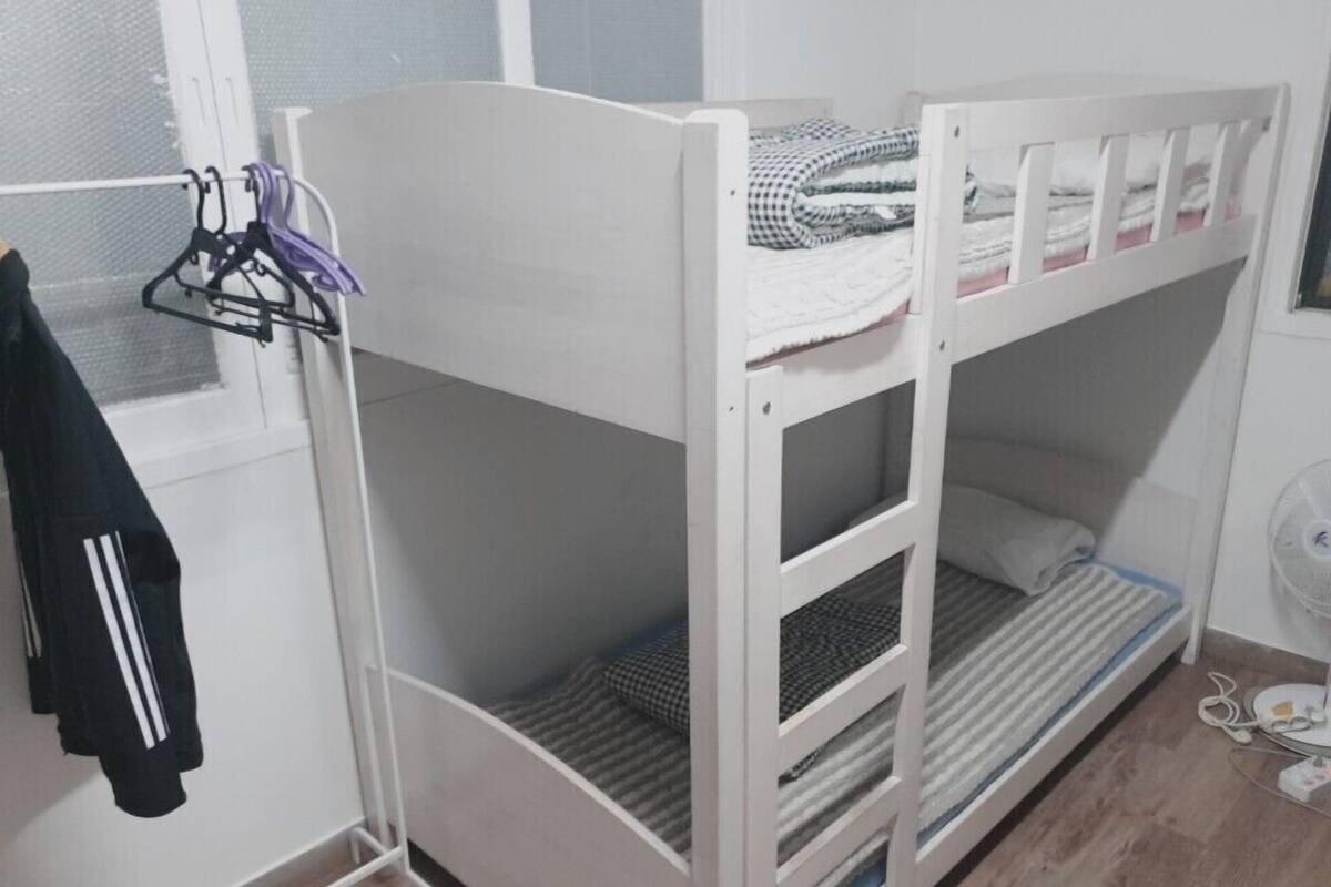 A bunk bed with a white frame, a window with a mesh screen, and a black jacket hanging on a hook.
