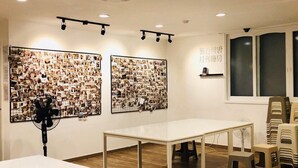 A room with wooden flooring, a white table, and two wall-mounted photo displays. - Orange Guesthouse - Hostel (Busan)