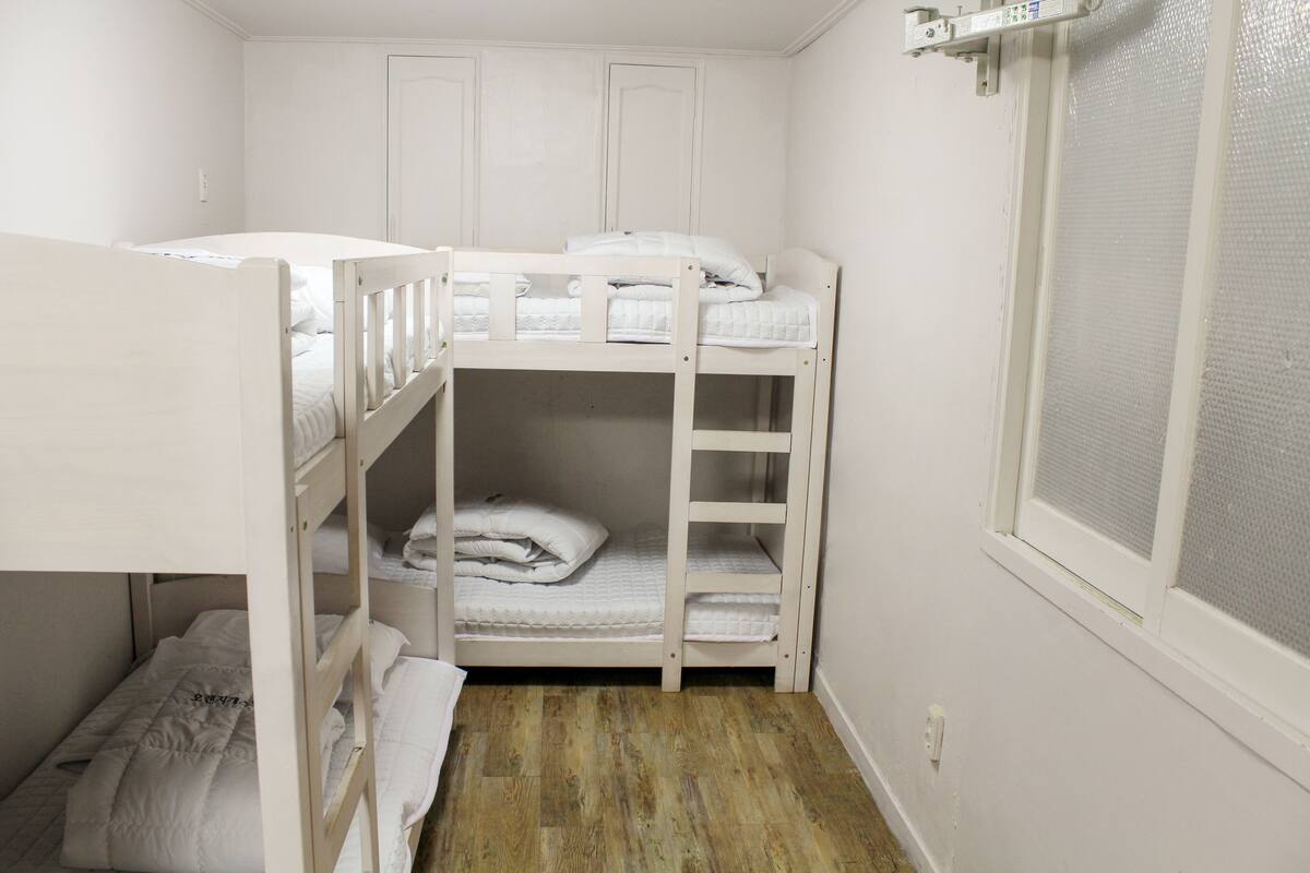 A bunk bed room with white bedding and a window with a mesh screen.