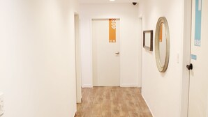 A hallway with wooden flooring, white walls, and a door with a blue sign. - Orange Guesthouse - Hostel (Busan)