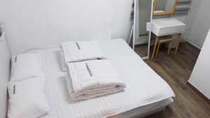 A neatly made bed with white bedding and pillows, a wooden chair, and a mirror in a room with white walls and wooden flooring. - Orange Guesthouse - Hostel (Busan)