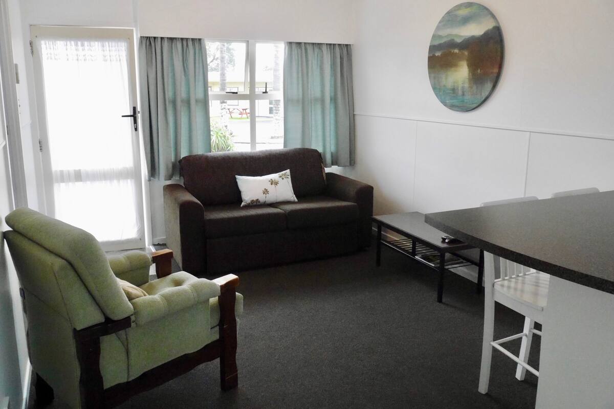 Una sala de estar con sofá, sillón, mesa de centro y un cuadro en la pared.