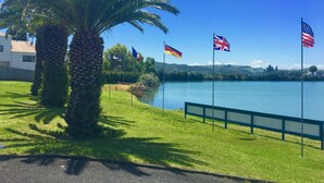 Fredfyldt søudsigt med palmer, en græsplæne og flag fra Storbritannien, Tyskland og USA.