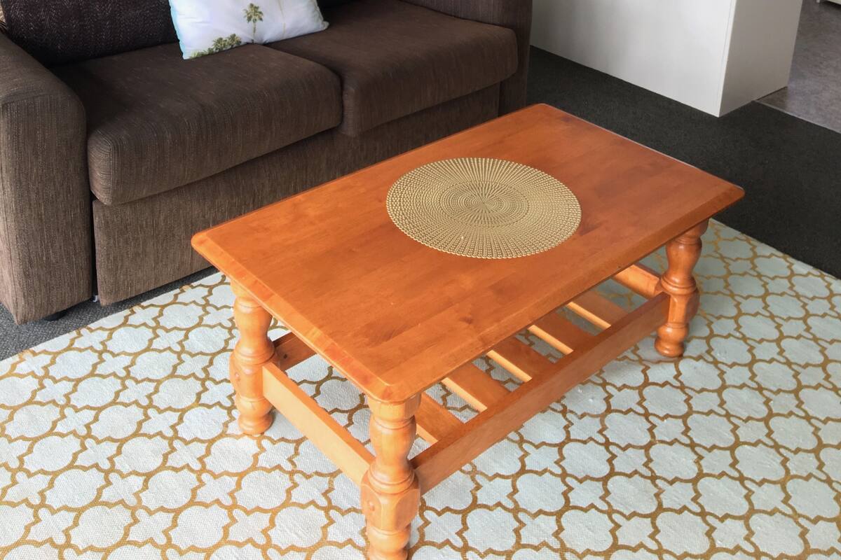 Una sala de estar con un sofá marrón, una mesa de centro de madera y una cocina con un fregadero y ventana.