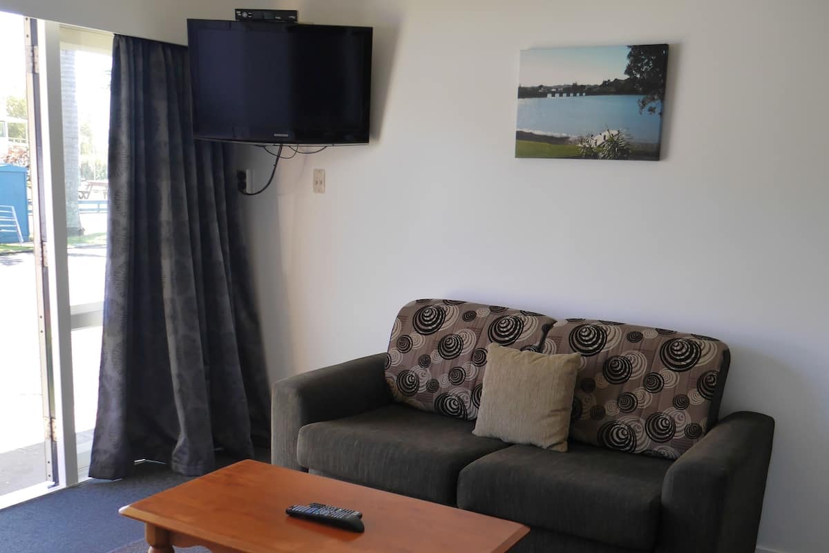 Una sala de estar con una mesa de centro de madera, un sofá gris con cojines estampados, un televisor montado en la pared y una ventana con cortinas.
