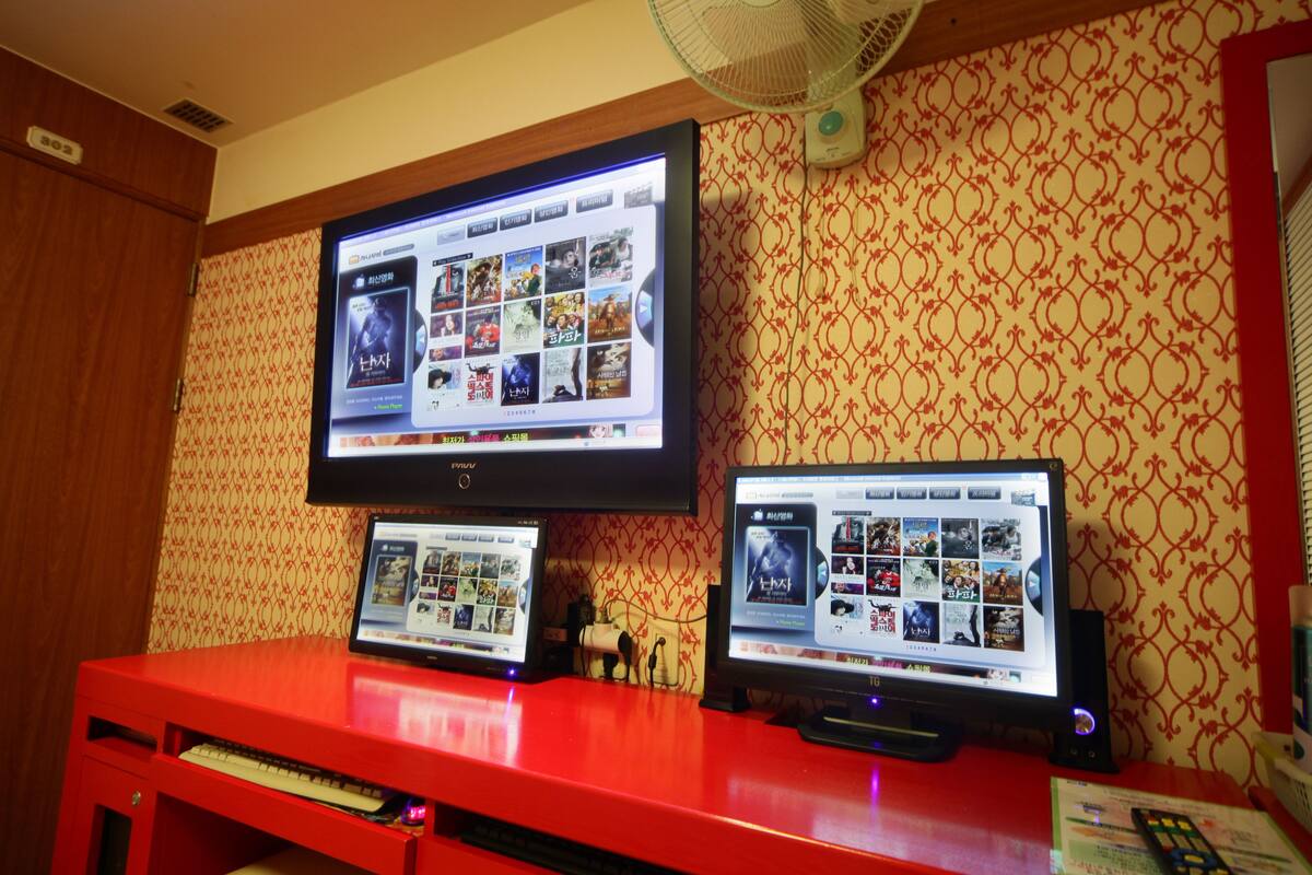 A room with a red desk, two laptops, and a television displaying a movie selection.